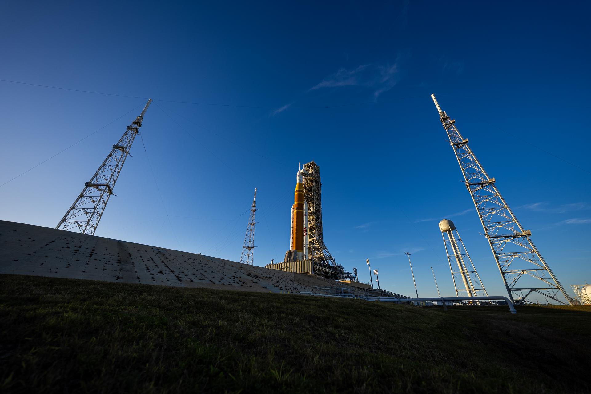 The sun sets on NASA’s Space Launch System (SLS) rocket and Orion spacecraft as they stand fully assembled atop the mobile launcher at Launch Pad 39B at NASA’s Kennedy Space Center in Florida. The sky glows with warm shades of orange and pink, silhouetting the towering rocket and its solid rocket boosters against the fading light.  Photographed on January 31, 2026, the scene captures teams preparing for a wet dress rehearsal for the Artemis II mission, rehearsing launch countdown timelines and procedures as day turns to night. 